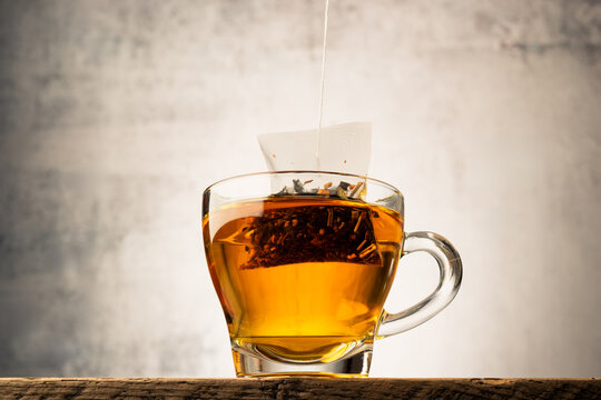 Glass cup of tea on wooden table with tea bag inside.