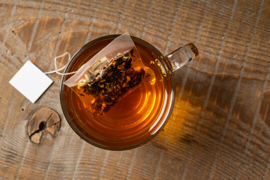 Glass cup of tea on wooden table with tea bag inside. Top view.