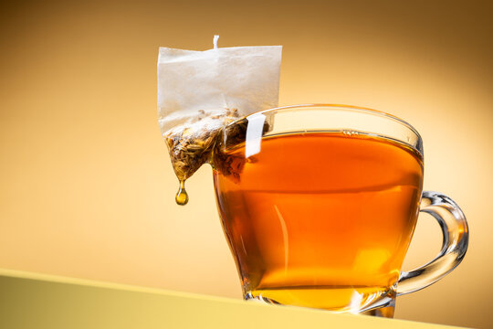 Glass cup of tea with dripping tea bag on yellow background