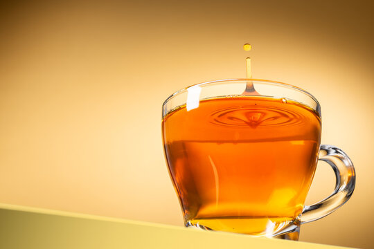 Glass cup of tea with splashing droplet on yellow background