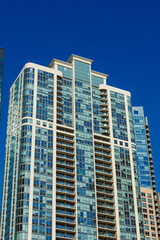 Fototapeta premium Urban landscape shows tall building with glass windows under clear blue sky during bright daylight in a busy city