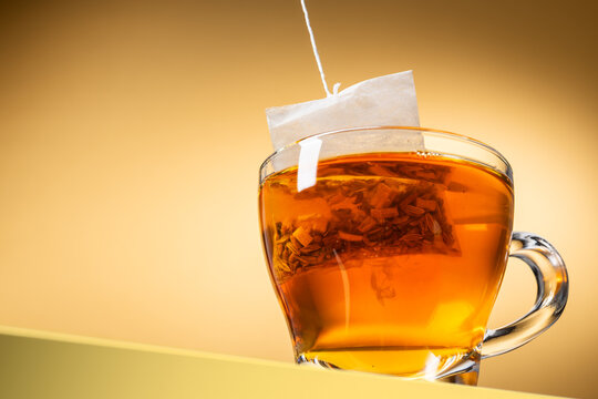Glass cup of tea with tea bag inside on yellow background