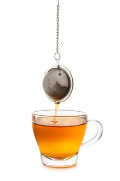 Glass cup of tea with dripping metal tea infuser, isolated on white background.