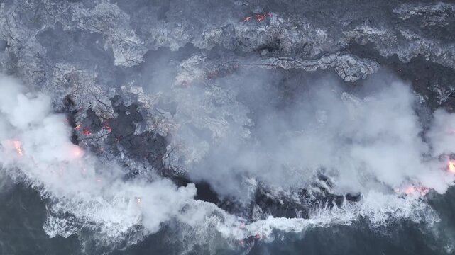 Aerial view of lava flowing into the ocean, with white steam contrasting against the dark volcanic rock, Piton de la Fournaise, Sainte Rose, Reunion.