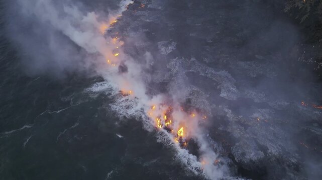 Aerial view of molten lava flowing into the ocean, creating steam and smoke against the dark water, Piton de la Fournaise, Saint-Benoit, Reunion.
