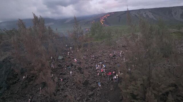 Aerial view of the dark volcanic landscape contrasting with the bright orange lava flow, with many people seen, Piton de la Fournaise, Saint-Benoit, Reunion.