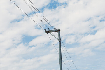 Fototapeta premium Electric utility poles stand against a cloudy sky in a rural area during midday with clear blue patches visible among the clouds