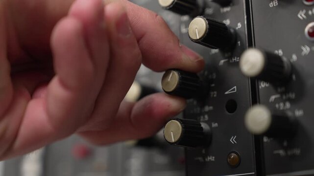 Close up of man's hand adjusting knob of retro audio mixer. Man turns the volume knob in a special device to make the music louder or quieter.