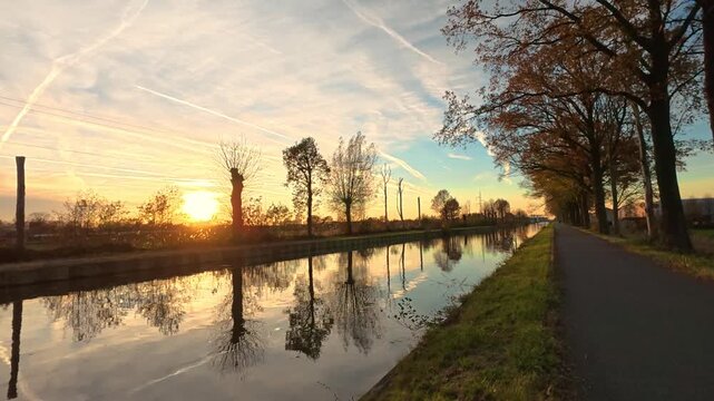 Tranquil Sunrise over a Rural Canal in Autumn with Perfect Water Reflections and Golden Sky
