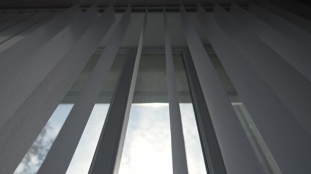 White vertical blinds gradually opening, filtering sunlight through window, creating cozy and atmosphere in room. blinds opening and closing, filtering sunlight through window