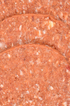 A detailed close up view shows the rough texture of three raw gourmet pljeskavica patties with visible white bits of fat and cheese