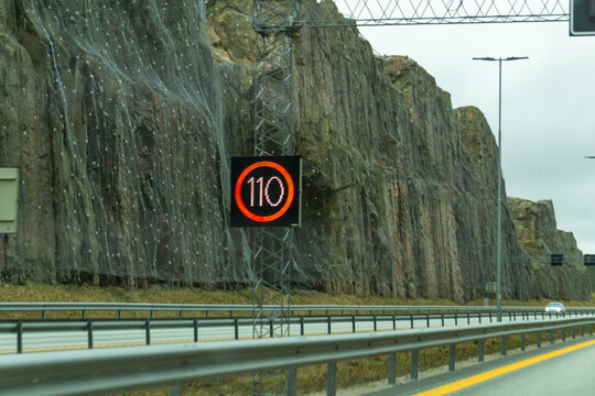 Digital 110 Variable Speed Limit Sign on Modern Norway Motorway with Rocky Cliff Face and Rockfall Protection Netting Background