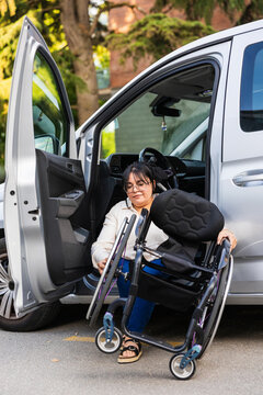 Woman assembling wheelchair beside adapted car in urban setting
