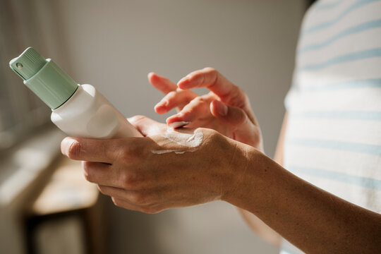 Hand applying cream from bottle indoors as part of skincare routine