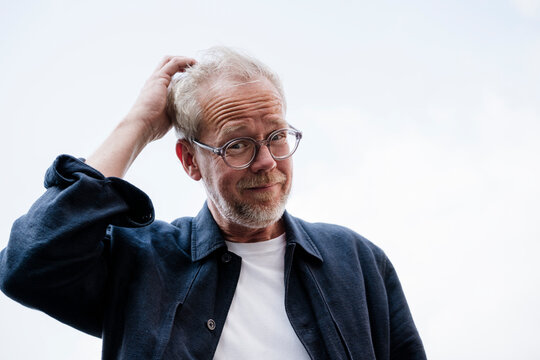 Portrait of bearded person with glasses scratching head outdoors