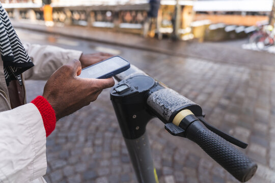 Man using smartphone to unlock electric scooter in urban street