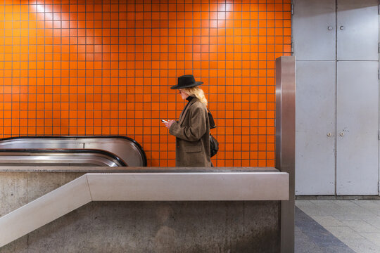 Young man with hat using smartphone while waiting in urban subway station