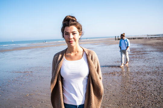 Smiling woman on sunny beach with second person in background