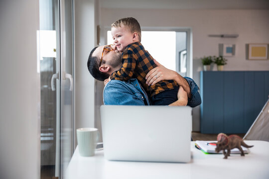 Father embracing son while working from home at desk