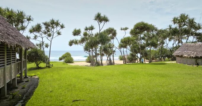 Traditional thatched roof bungalows on green grass meadow, tranquil tropical escape with serene white sand beach coast and the Pacific Ocean. Travel to Port Resolution, Tana Island exotic resort