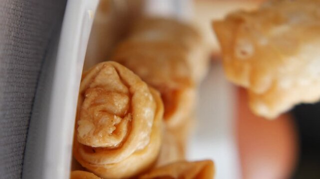 Crispy golden fried banana pastry snack being picked up from white plate in vertical video.