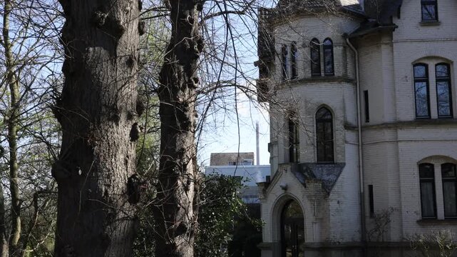 Closer architectural shot of the old house highlighting facade details with an industrial chimney softly visible behind it.