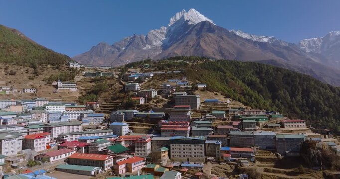 Aerial shot of Namche Bazaar Nepal showing colorful rooftops in an amphitheater-shaped settlement surrounded by green forest, rugged hills and snow-capped Everest Himalayan peaks