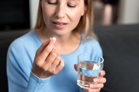 Young woman prepares to take medication with water at home in the living room