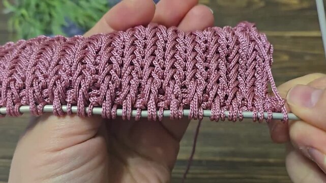 A textured, openwork knitting pattern made with colored yarn on a wooden surface with decorative flowers. Close-up of the knitting texture and pattern. Conceptual ideas for handicrafts