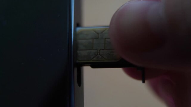 Person inserting a sim card into back of mobile phone, Sim card in tray being inserted into phone, closeup