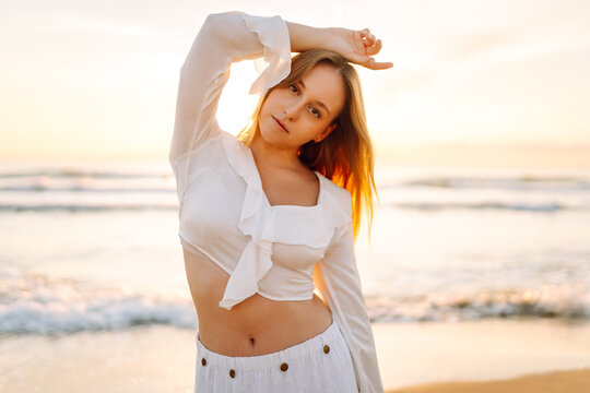 A young woman strolls along the beach at sunset. A beautiful woman enjoys the sea breeze and relaxes outdoors. A concept of beauty, relaxation, and nature.