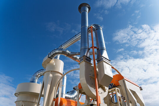 Industrial air filtration and cyclone dust collector system at a grain processing facility, heavy duty ventilation pipes and agricultural machinery under blue sky