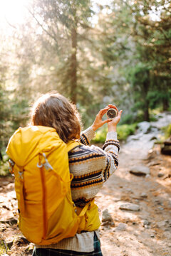 Rear view of young woman with hiking backpack holding compass while standing on hiking trail in mountains. Woman holds compass and looks for directions while hiking. Navigation concept, hiking.