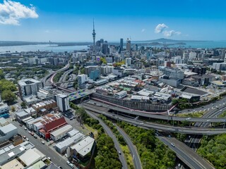 Obraz premium Aerial view of Auckland, New Zealand, showcasing the city skyline with the Sky Tower, buildings, and harbor. Cars travel on the highway, illustrating urban transportation.