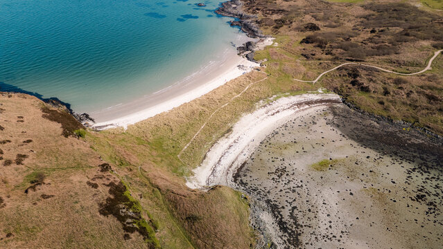Aerial view of the pristine Twin Beach where turquoise waters meet the rugged coastline, Isle of Gigha, Argyll and Bute, Scotland.