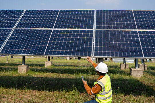 Field technician checking ground-mounted photovoltaic panels, using handheld device while adjusting array alignment, ensuring stable performance and efficient energy generation in outdoor conditions.