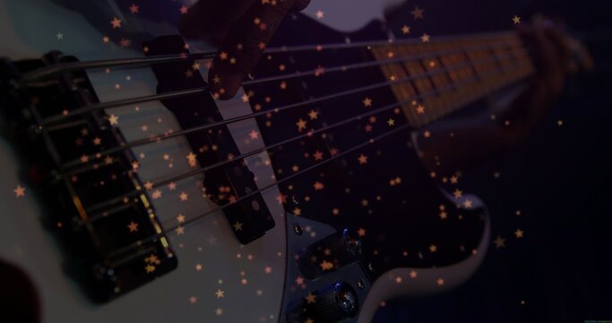 Plucking musician's hand in dark sleeve moving along bass guitar strings at studio, with star bokeh