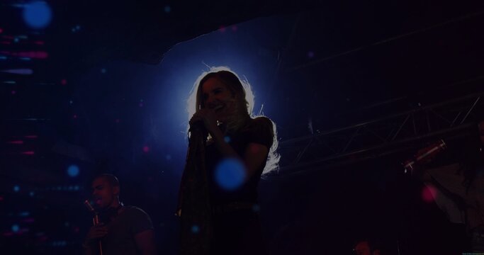 Singing lead vocalist wearing dark top on dim concert stage, backlit halo, left singer holding mic