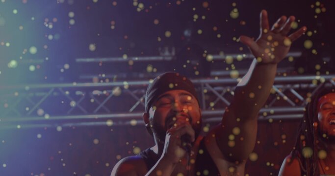 Singing lead singer wearing beanie tank top holding mic, raising arm on concert stage with confetti