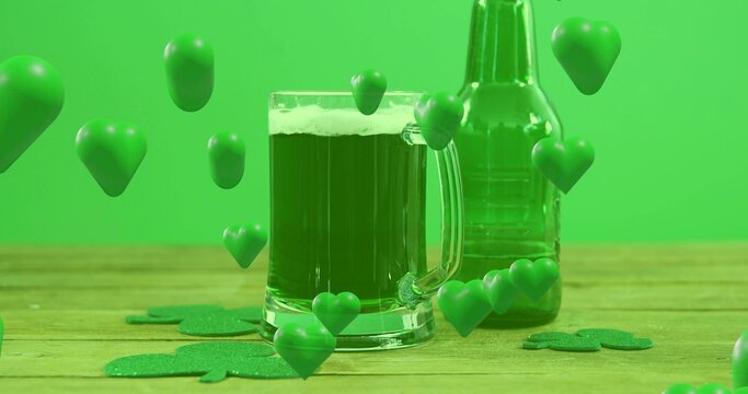 Displaying glass mug with green beer, foam on wooden tabletop with green bottle, shamrocks, hearts