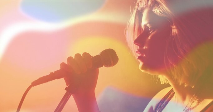 Singing teen holding wired mic under stage lights, wearing sleeveless top and necklaces, copy space