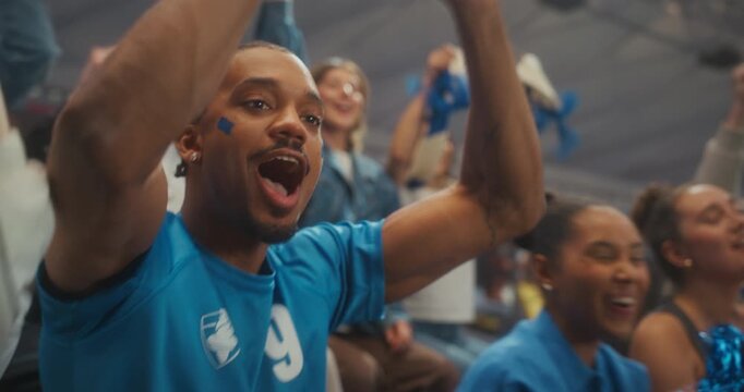 Portrait of a Young Black Male Supporter in a Blue Jersey Cheering With Smiling Fans in a Packed Stadium During a Professional Soccer League Match, Celebrating a Major International Championship.