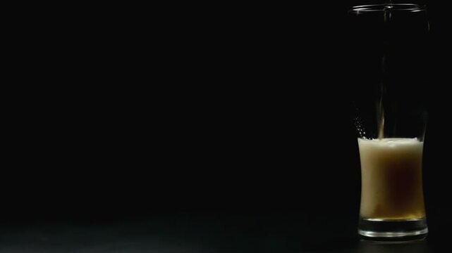 Foamy beer is poured into a large glass on a black background, space for text