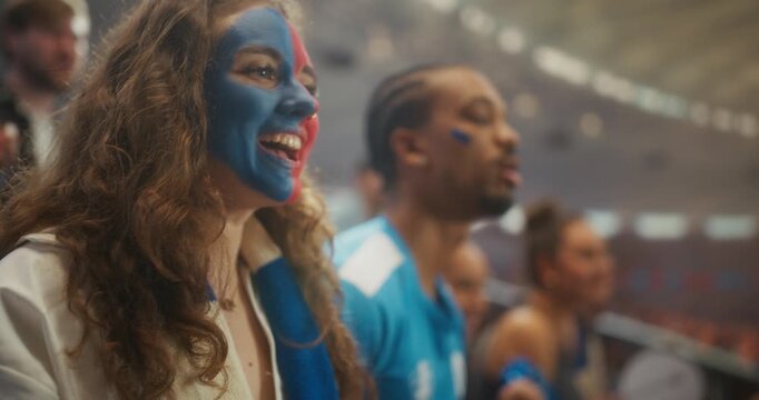 Close-up of a Young Woman With Blue and Red Face Paint Smiling and Chanting Beside a Black Male Supporter, as Happy Football Fans Celebrate a Professional International League Match Game in Stadium.