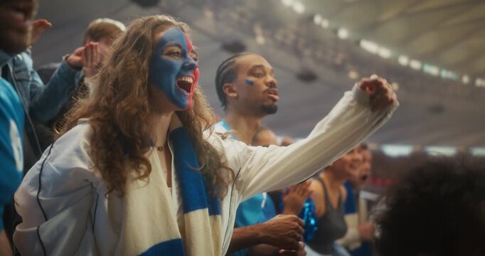 Portrait of Jubilant Soccer Supporters in a Packed Stadium as a Young White Woman With Blue and Red Face Paint Smiles, Shouts and Lifts Her Arms Beside a Black Male Fan During a Major League Cup Match