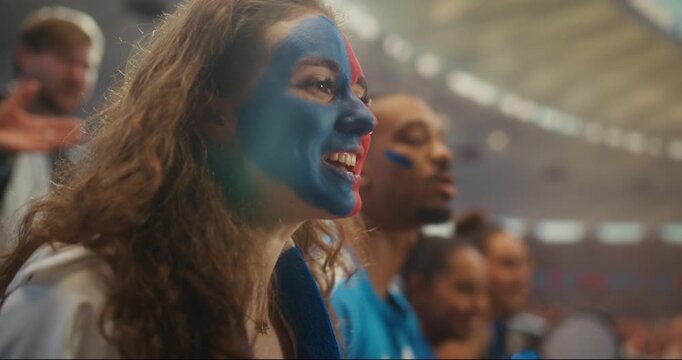 Portrait of Joyful Football Supporters at a Professional International League Match. Portrait of Young White Woman With Blue and Red Face Paint Smiling, Cheering and Raising Her Arms
