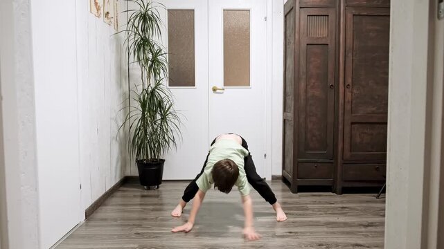 Caucasian boy doing an exercise stretching his body, bending forward and touching the floor with hands at home interior. Strengthening the muscles of arms, back, hips, legs and shoulder girdle. 4K.