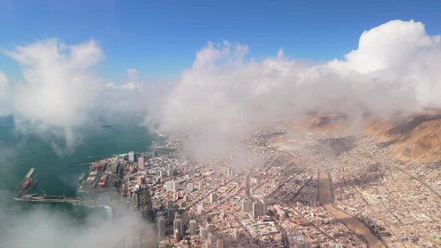 4K drone flight over camanchaca fog in Antofagasta, Chile. Cinematic reveal of the city and Pacific Ocean through white clouds under a clear blue sky. Ideal for documentaries and travel.