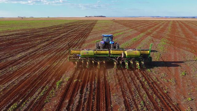 Blue tractor pulling multi-row precision planter in Formosa, Goi&aacute;s, Central-West Brazil, creating uniform planting rows with accurate spacing in mechanized agriculture, drone follow push in shot.