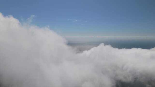 Cinematic 4K drone flight approaching a massive, towering wall of white coastal clouds over the Pacific Ocean. High altitude perspective showcasing the vast scale of nature